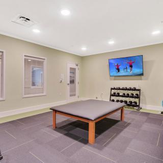 A modern home gym with a mounted television, dumbbells on a rack, and ample space for exercise.
