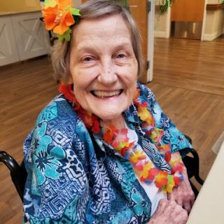 A joyful elderly woman dressed in colorful attire, adorned with flowers, enjoying a cheerful moment.