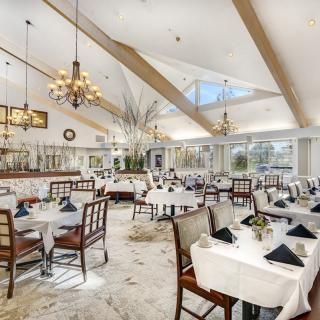An elegant restaurant dining area with chandeliers, white tablecloths, and neatly arranged tables and chairs.
