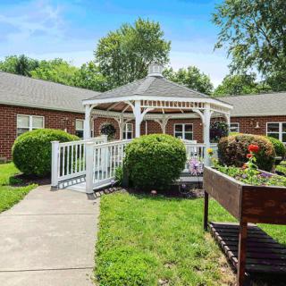 A charming gazebo in a garden setting with a pathway leading to it, surrounded by greenery and adjacent to a brick building.