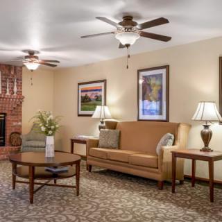 A cozy living room featuring a sofa, chairs, wooden tables, brick fireplace, ceiling fans, and warm lighting.
