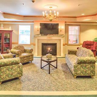 A cozy living room featuring a fireplace, sofas, and armchairs arranged around a central table, with a television mounted above the fireplace.