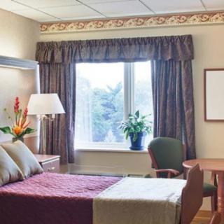 A well-lit hospital room with a bed, chair, and window adorned with curtains.