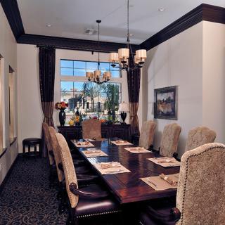 An elegant dining room with a large table, high-backed chairs, and a chandelier, featuring a window view.