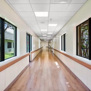 An empty hospital corridor with wooden floors and large windows.