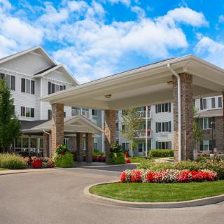 A well-maintained residential building with a landscaped entrance and vibrant flowers under a bright, cloudy sky.