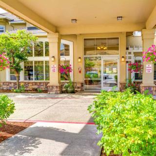 A well-maintained building entrance with glass doors, surrounded by lush greenery and columns.