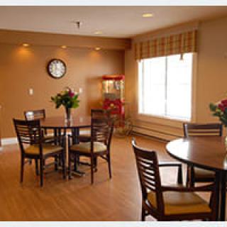 A cozy dining area with tables and chairs, a wall clock, and natural light coming through the window.