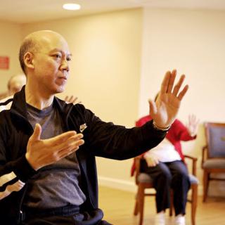 An elderly man practicing Tai Chi indoors, focusing on his movements for relaxation and wellness.
