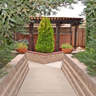 A serene garden pathway leading to a pergola, surrounded by lush greenery and potted plants.