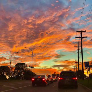 A vibrant sunset paints the sky with hues of orange and blue, as cars line up on the road.