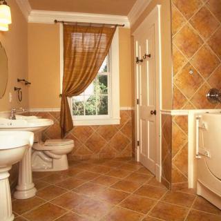 A warmly designed bathroom with tiled walls and floor, featuring a sink, toilet, and a window with drapes.