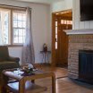 A cozy living room with a fireplace, sofa, and coffee table, featuring hardwood floors and a large window.