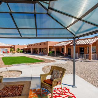 A comfortable outdoor seating area under a canopy, overlooking a well-maintained lawn and surrounded by buildings on a sunny day.