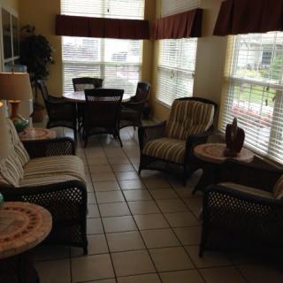 A cozy living room with wicker furniture, tiled floors, and large windows.