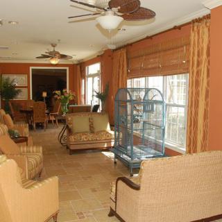 A cozy living room with warm colors, featuring comfortable seating, a ceiling fan, large windows with curtains, and a bird cage.