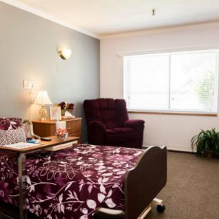 A cozy room with a hospital bed and armchair by the window.