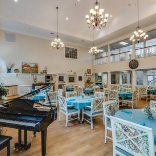 A spacious and elegantly designed dining area featuring a grand piano and chandeliers, with tables set for guests.