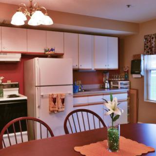 A cozy kitchen with a dining table and chairs, featuring a refrigerator and stove.