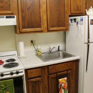 A compact kitchen setup featuring a stove, sink, and refrigerator with wooden cabinets.