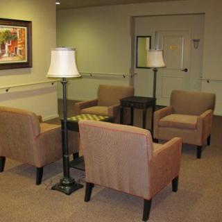 A cozy waiting area with four chairs, two lamps, and a central table on a carpeted floor.