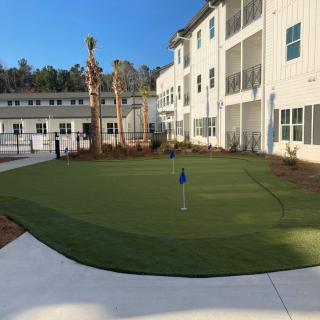 A residential building with an outdoor putting green surrounded by landscaped areas.