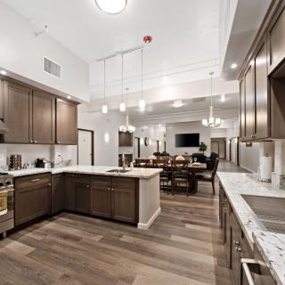 A modern kitchen with wooden cabinets and marble countertops, featuring an open layout and bright lighting.