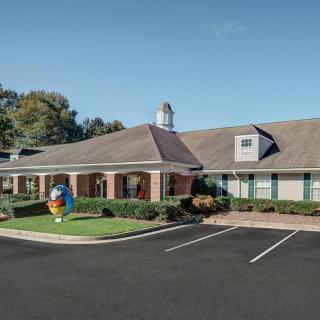 A brick building with a small parking lot and manicured landscaping under a clear blue sky.