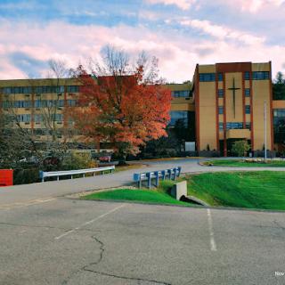 A picturesque view of a campus building surrounded by vibrant autumn foliage under a colorful sky.