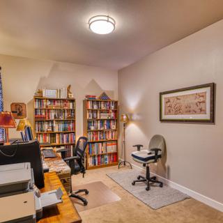A cozy home office featuring bookshelves filled with books, a desk with a computer chair, and decorative artwork on the wall.