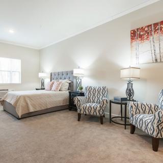 A modern bedroom with a large bed, decorative armchairs, and stylish lamps.