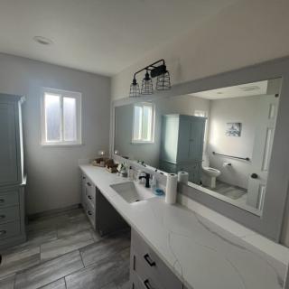 A modern bathroom with a large mirror, dual sinks, a window, and tiled flooring.