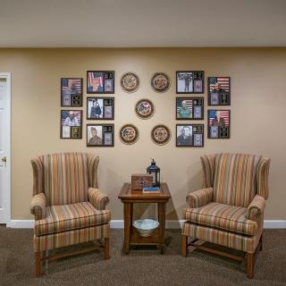 A cozy living room setup featuring two striped armchairs, a wooden side table, and a wall adorned with photo frames and decorative plates.