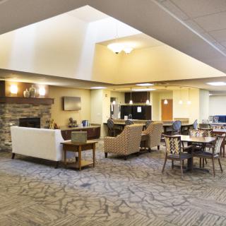 A spacious living room area with comfortable seating, tables, and natural lighting.