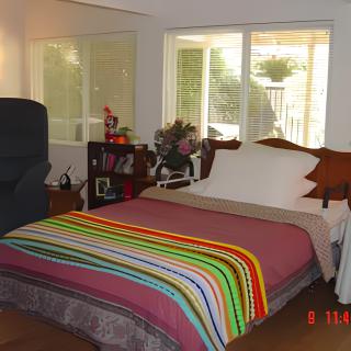 A cozy bedroom with a bed covered in a colorful striped blanket, surrounded by furniture and illuminated by natural light from the windows.