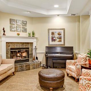 A cozy living room featuring a fireplace, piano, and comfortable seating with decorative artwork on the walls.