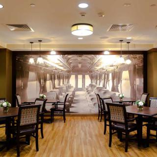An elegant dining area with tables and chairs, featuring a mural of a classic train interior.
