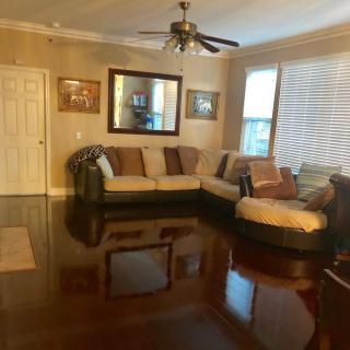 A cozy living room with a large sofa, hardwood flooring, and a ceiling fan.