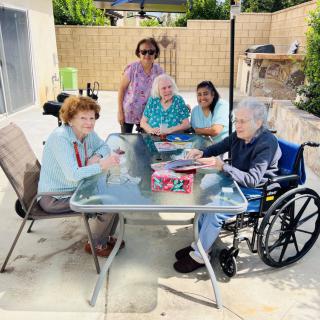 A group of seniors and caregivers enjoying time together outdoors around a table.