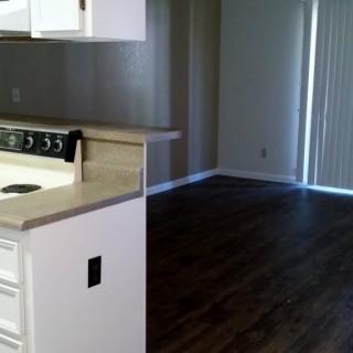 An empty apartment interior with a kitchen area and hardwood floors.