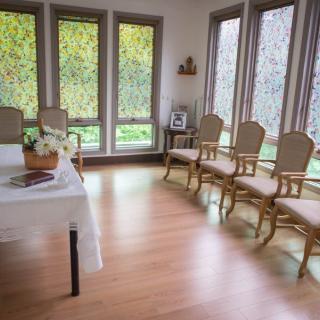 A serene, light-filled room with elegant chairs lined up against the walls and a table adorned with flowers.