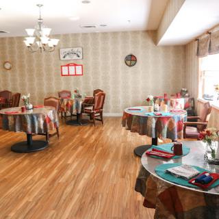 A cozy dining room with elegantly set tables and chairs, featuring warm lighting and classic decor.