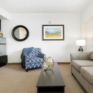 A cozy living room with a sofa, armchair, and coffee table, decorated with wall art and a mirror.