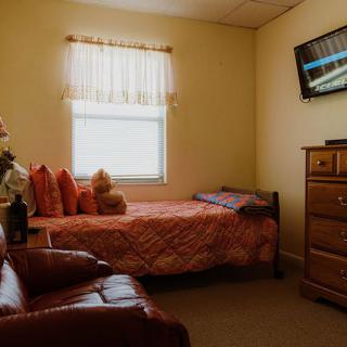 A cozy bedroom with a single bed, television, and dresser.