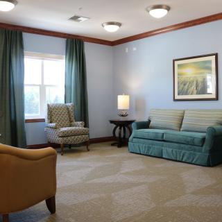 A cozy living room with a sofa, armchair, and a table lamp by the window.