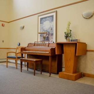 A room interior featuring a piano, bench, chair, and podium with wall art and a decorative plant.