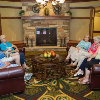 A group of seniors seated in a lounge area, engaging in conversation near a fireplace.