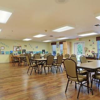 A spacious dining area with multiple tables and chairs, featuring wooden flooring and bright lighting.