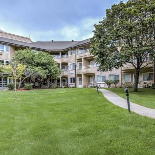 A residential apartment building with a well-maintained lawn and surrounding trees.