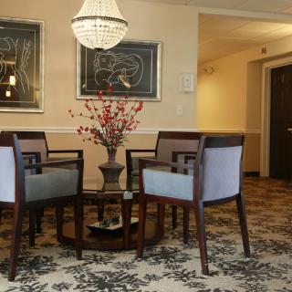 A cozy living room area with elegant chairs and a table, decorated with a chandelier and artwork on the walls.